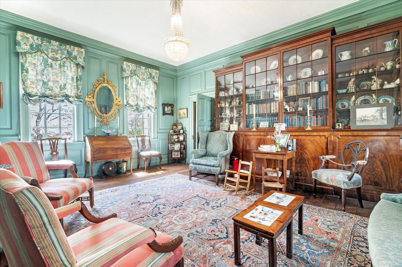The green drawing room, where painted paneled walls, tall period windows, and a crystal chandelier brighten the historic interior.