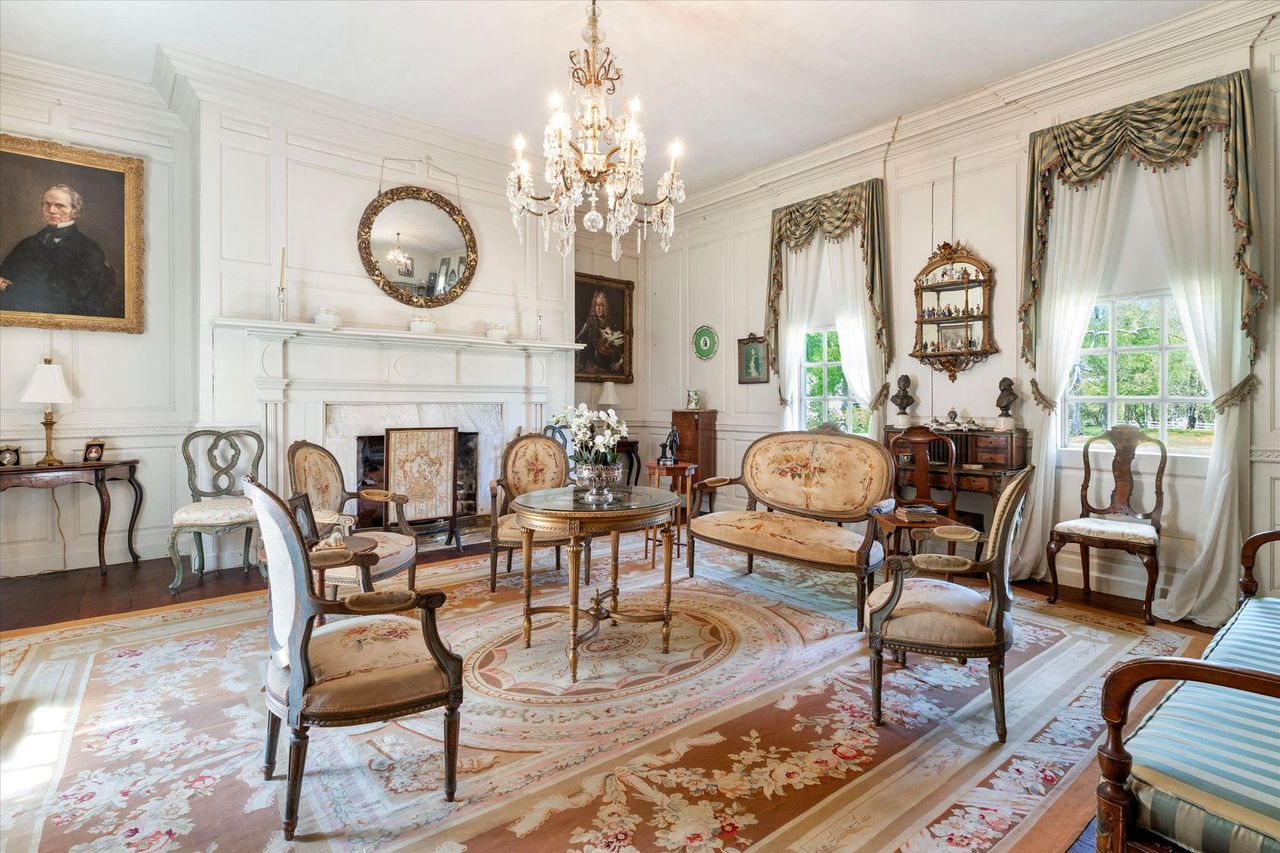The formal salon feels lighter and more refined, with white paneled walls, soaring ceilings, and a marble fireplace.