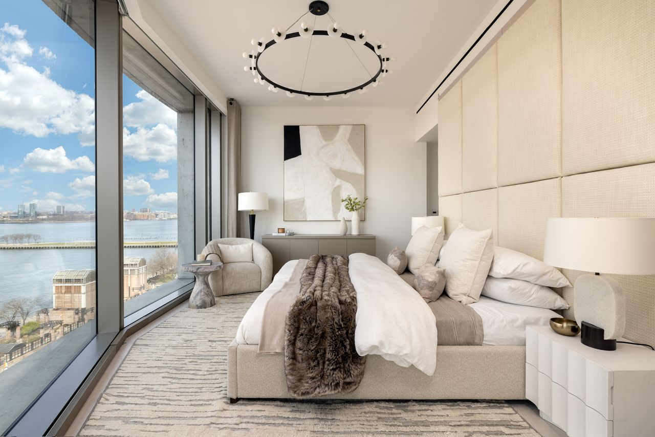 Bedroom is set against a fully upholstered headboard across from floor-to-ceiling windows. 