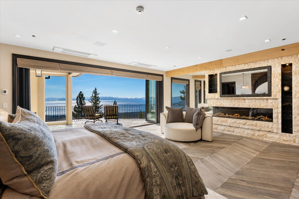 On the far wall, retractable panoramic glass doors open the room onto a private terrace overlooking Lake Tahoe, while a linear stone fireplace with a two-way mirrored television adds warmth.