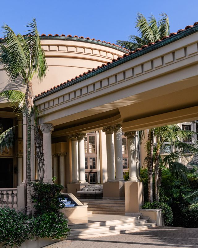 Surrounded by dense tropical landscaping and Mediterranean-inspired architecture, the entrance starts with a small covered lounge before arriving at the front door.