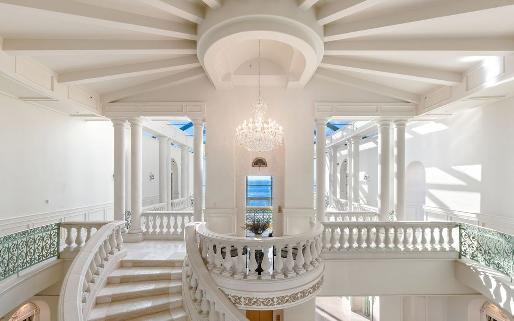 White marble floors, carved balustrades, and fluted columns give the staircase a classical feel.
