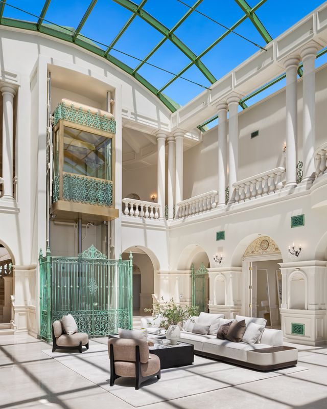 A spacious lounge is arranged beneath the atrium beside a glass elevator that connects the home's multiple levels. 