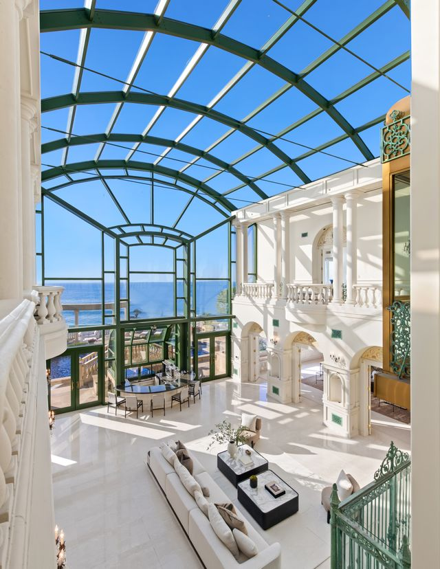A dramatic two-story sunroom where soaring glass walls stretch from floor to ceiling, framing views of the Pacific Ocean. 
