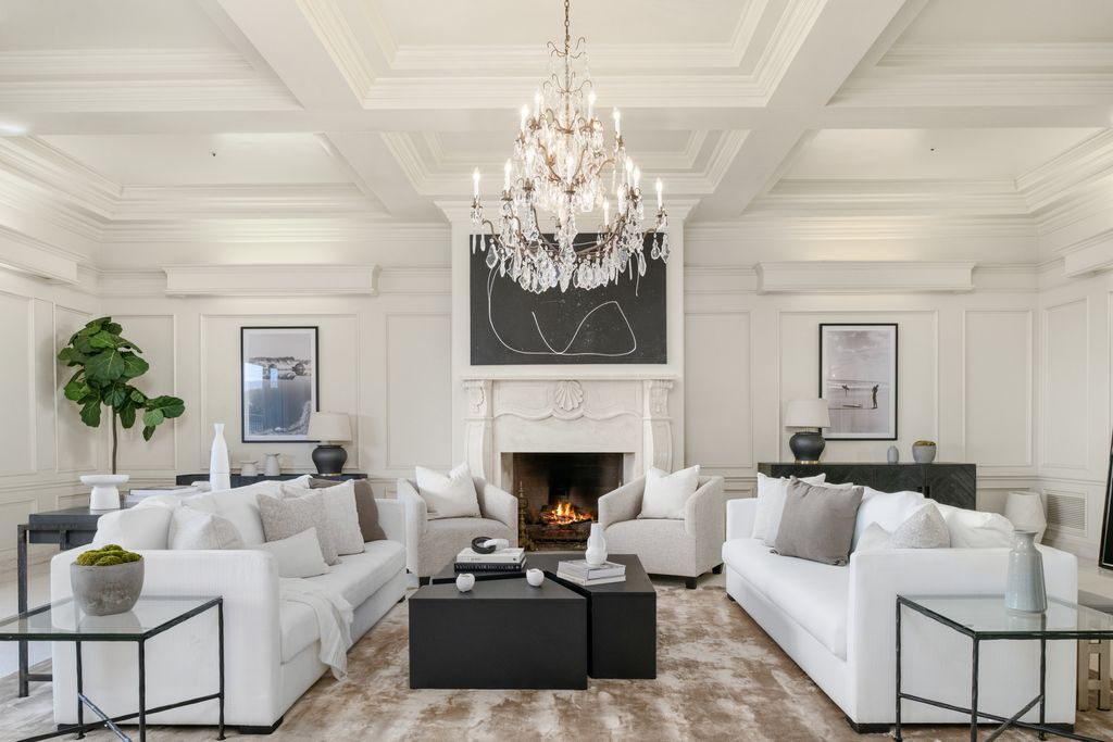 A crystal chandelier hangs above two facing sofas and a pair of armchairs arranged around the fire.