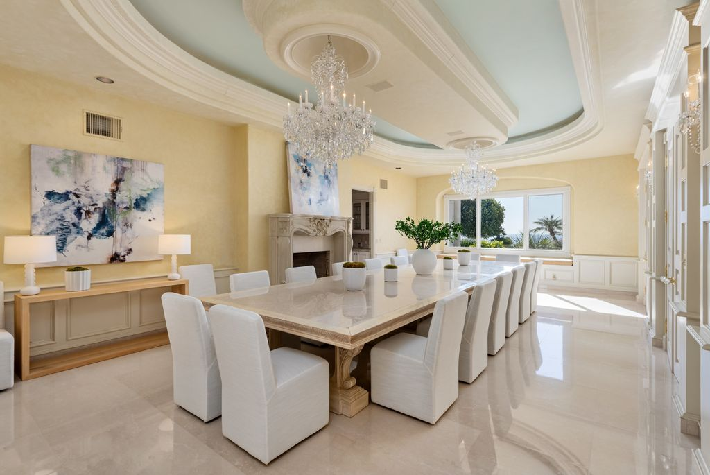 A long stone dining table is in the center of the room, while a carved fireplace and oversized picture window add warmth to the space.