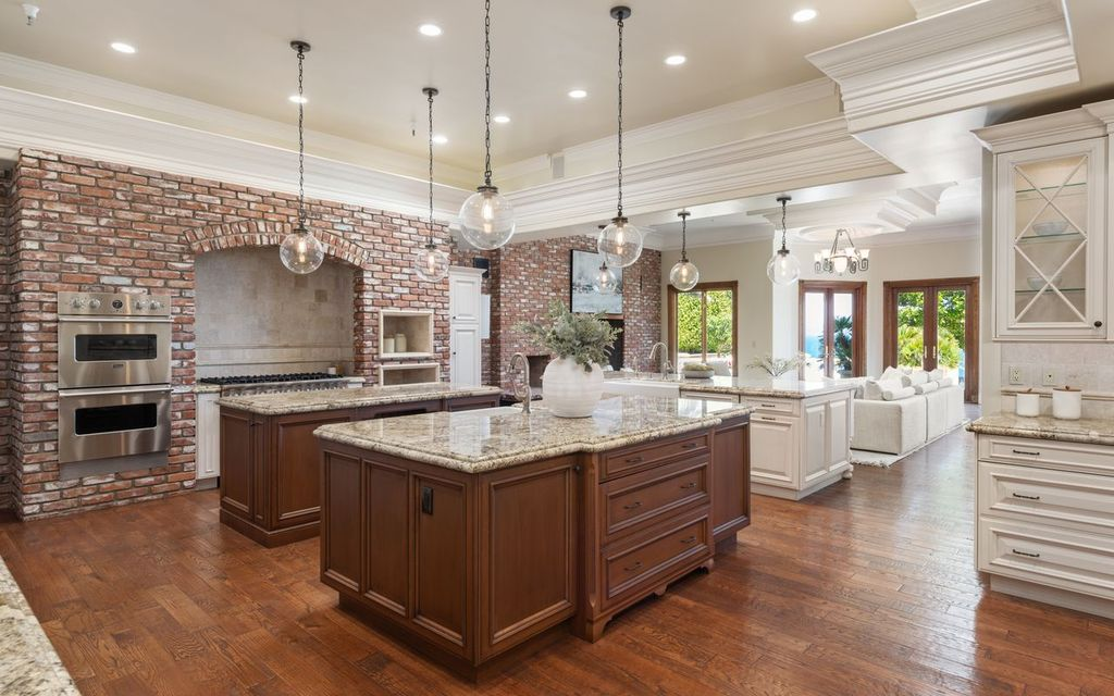 Two granite-topped islands provide prep and gathering space, while a large brick cooking alcove frames a professional-grade range.