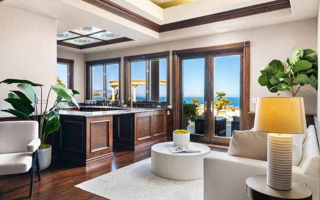 Dark wood cabinetry and stone countertops frame the bar, while French doors open onto an ocean-facing terrace.