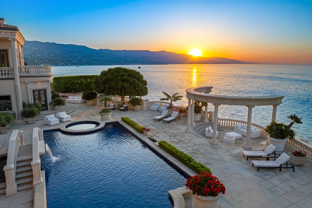 A large rectangular pool stretches toward the water with a circular spa positioned at one end. 
