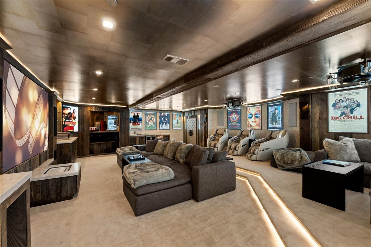 Inside, the room features a large projection screen, deep sectional seating, massage chairs, soft rope lighting, and a dedicated popcorn station.