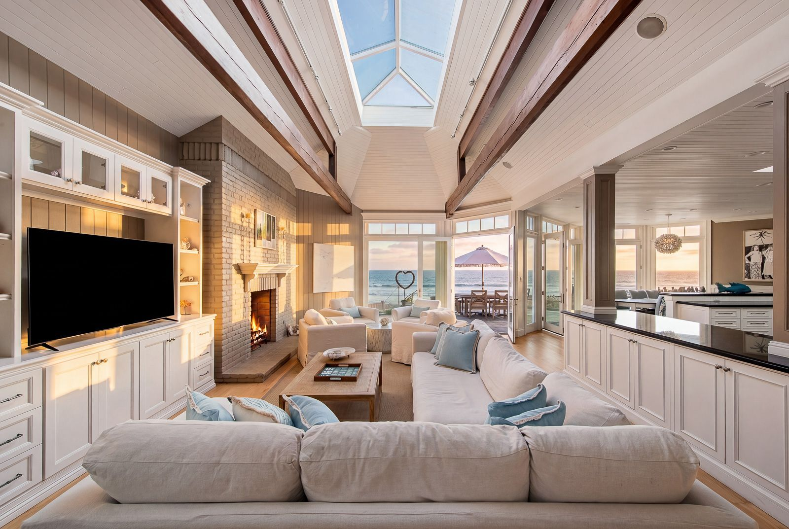 At the center of the living area, a painted brick fireplace is framed by custom built-ins and surrounded by oversized sofas and lounge chairs arranged to face both the fire and the water. 