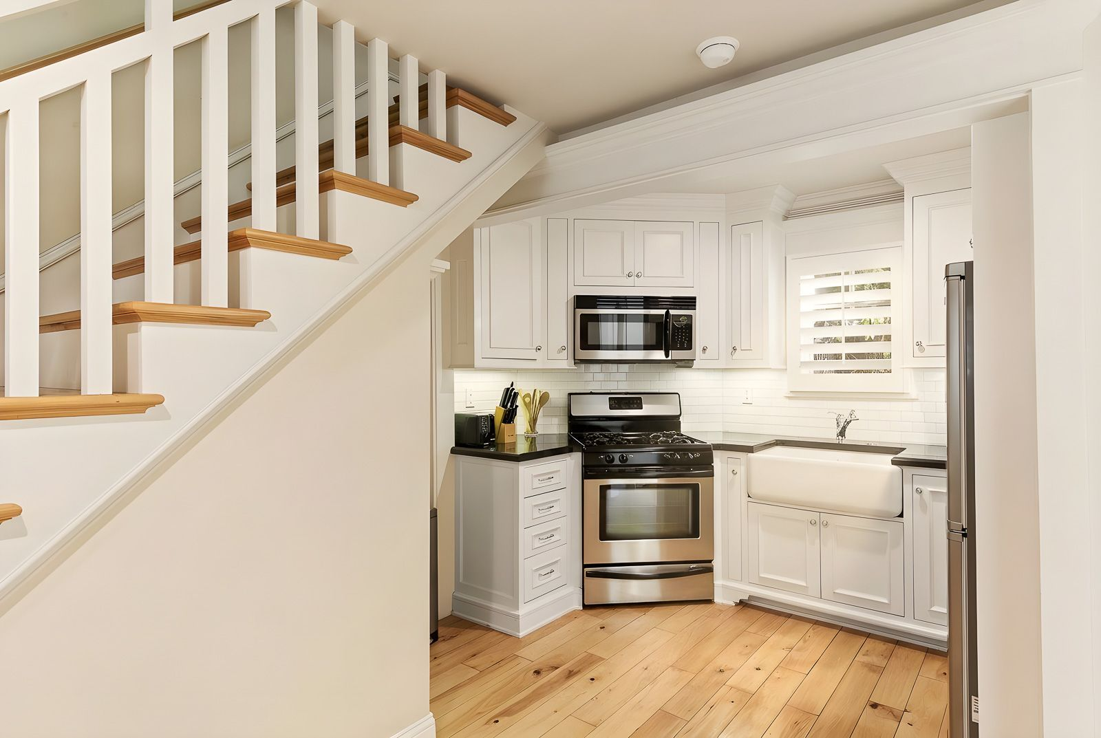 Around the corner, a full kitchen is equipped with white shaker cabinetry, black stone countertops, stainless steel appliances, and a farmhouse sink.