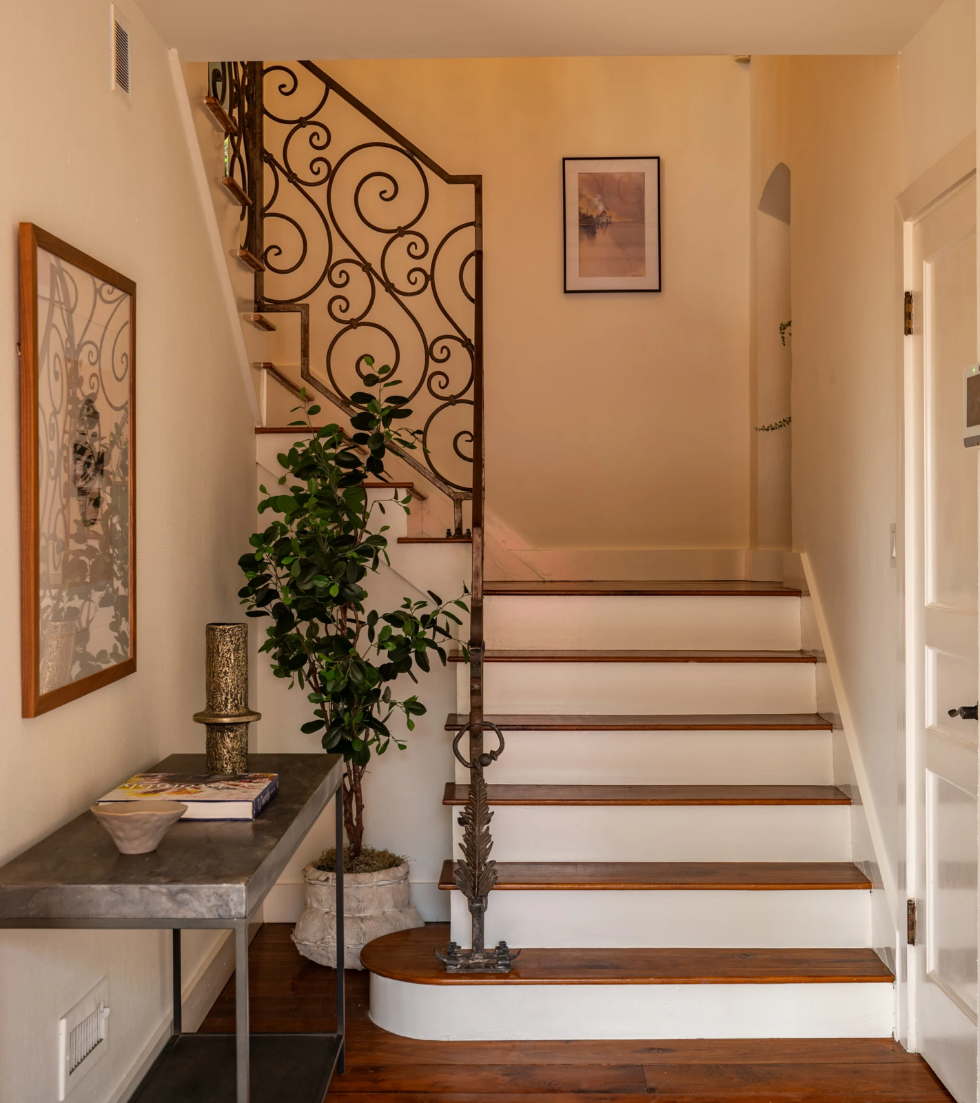 Entrance lined with dark wood flors where a staircase takes up most of the space. 