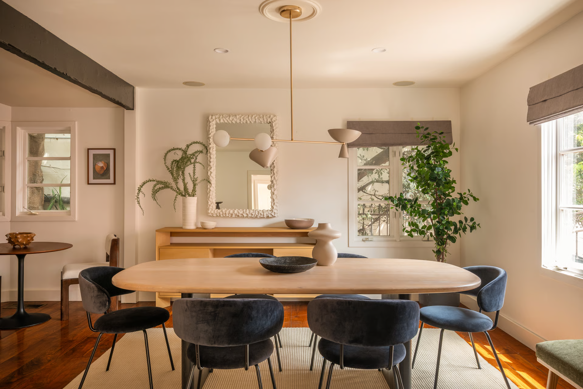 A more intimate dining space centered around a sculptural wood table beneath a modern brass light fixture. 
