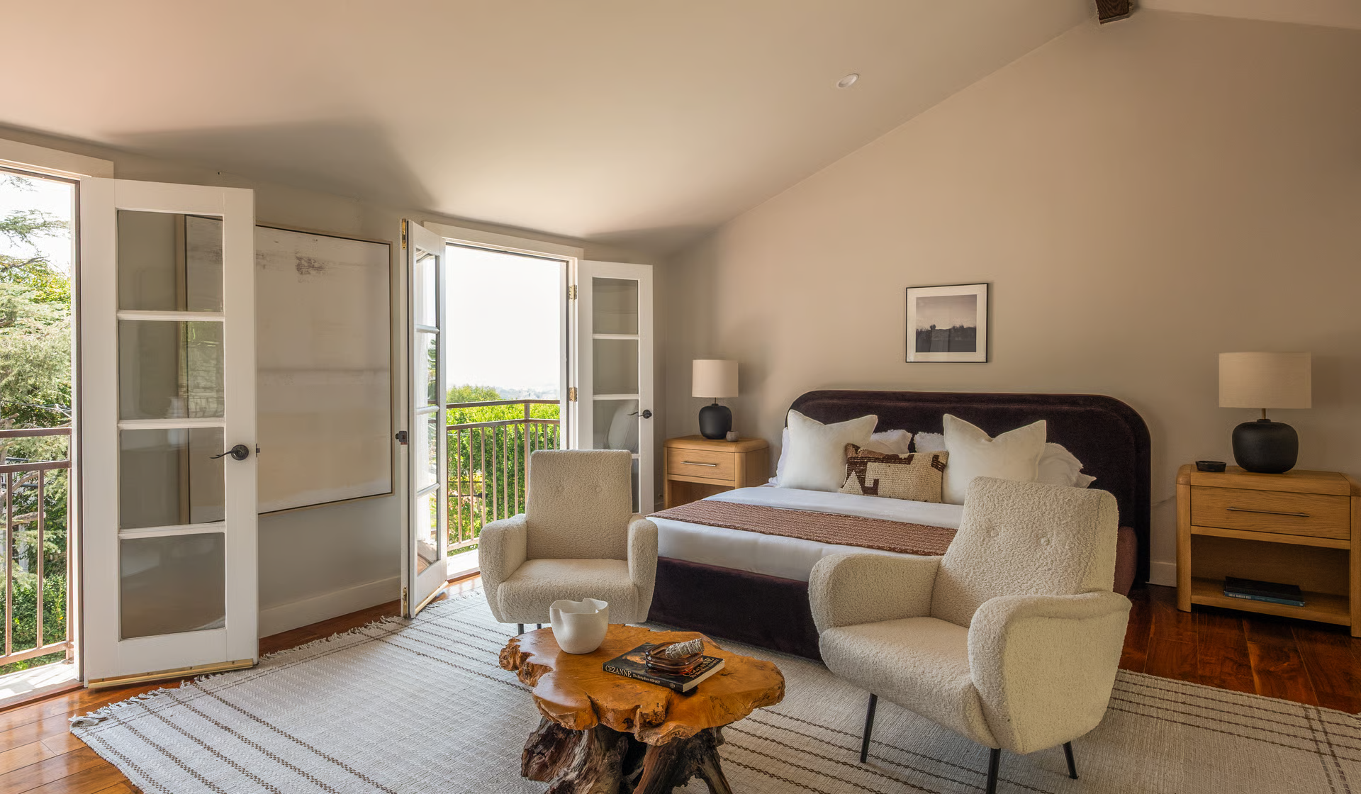 A spacious bedroom that feels bright and airy, with a plush upholstered bed and a cozy sitting area positioned to take advantage of the natural light. 
