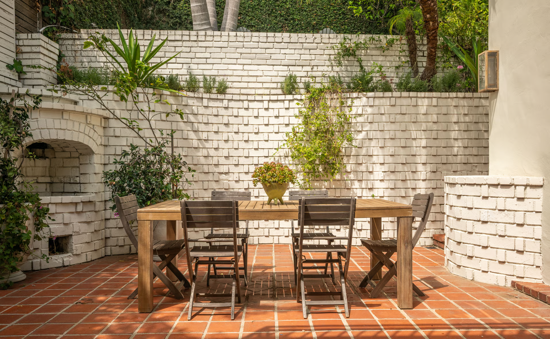 A brick dining terrace with a built-in wood-fired oven tucked into one corner and a large dining table at the center of the patio.