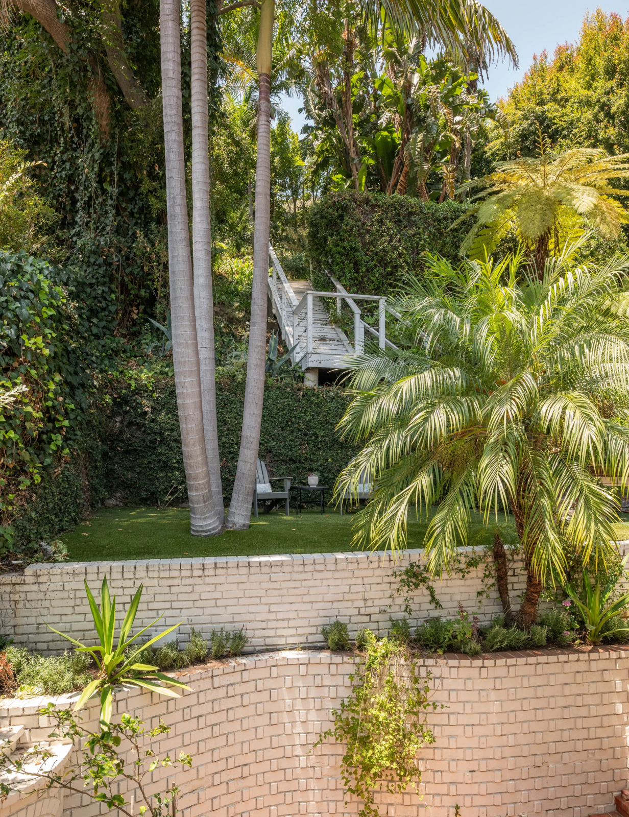 Raised white brick planters soften the edges of the space, giving the courtyard a secluded, garden-like feel, which continues up a set of steps that leads to the next level of the backyard. 