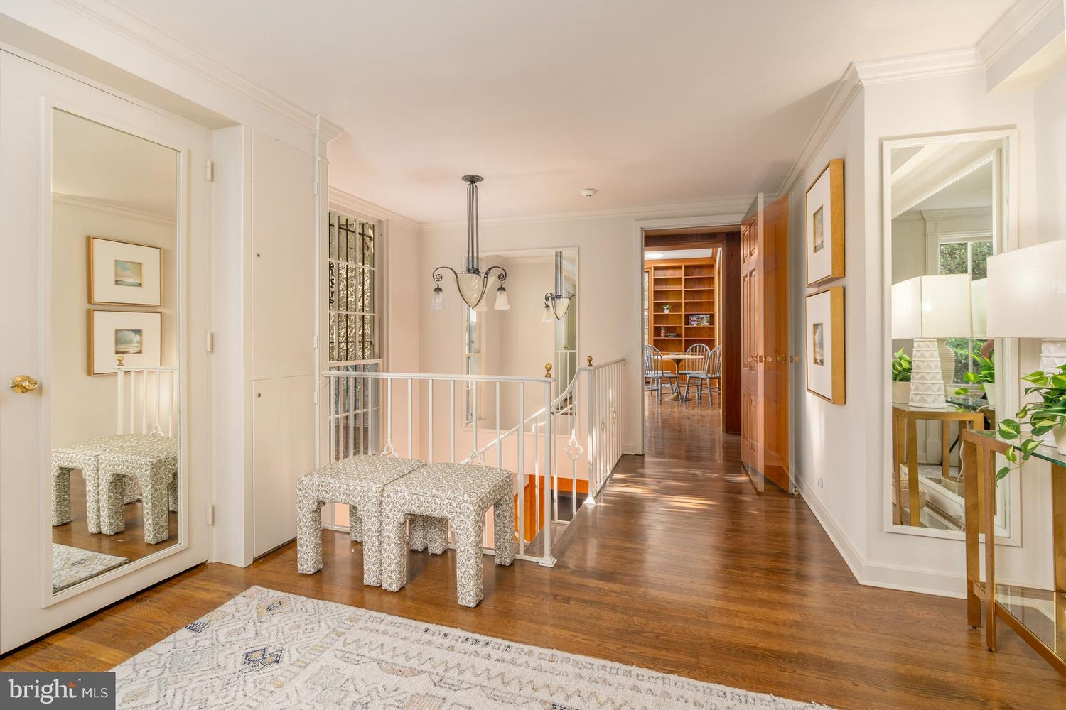 Warm hardwood floors lead across the entry toward a central stairwell, while mirrored doors and pale walls help the space feel even more open.