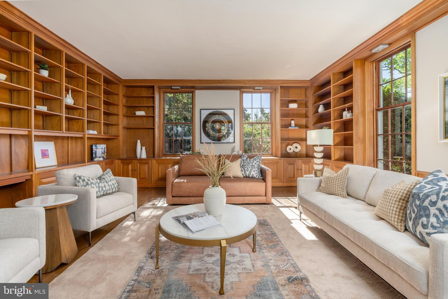 A library with floor-to-ceiling built-in bookshelves that wrap nearly every wall in warm wood, interrupted only by tall divided-light windows.