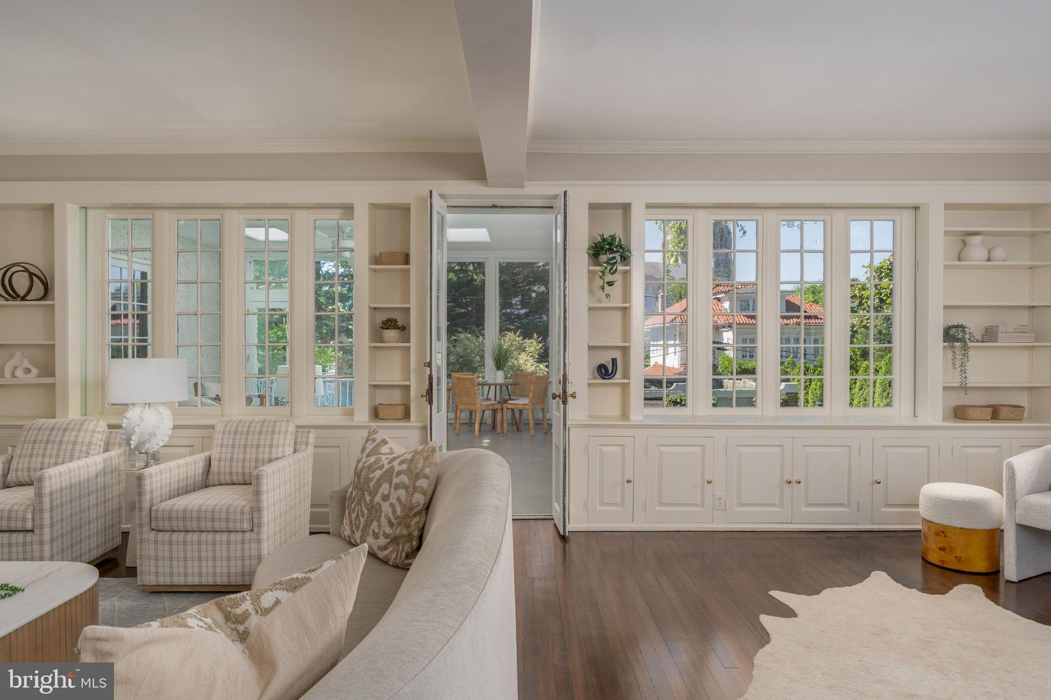 A wall of divided-light windows and built-in cabinetry stretches across one side of the room, keeping the connection to the sunroom and gardens while filling the space with natural light.