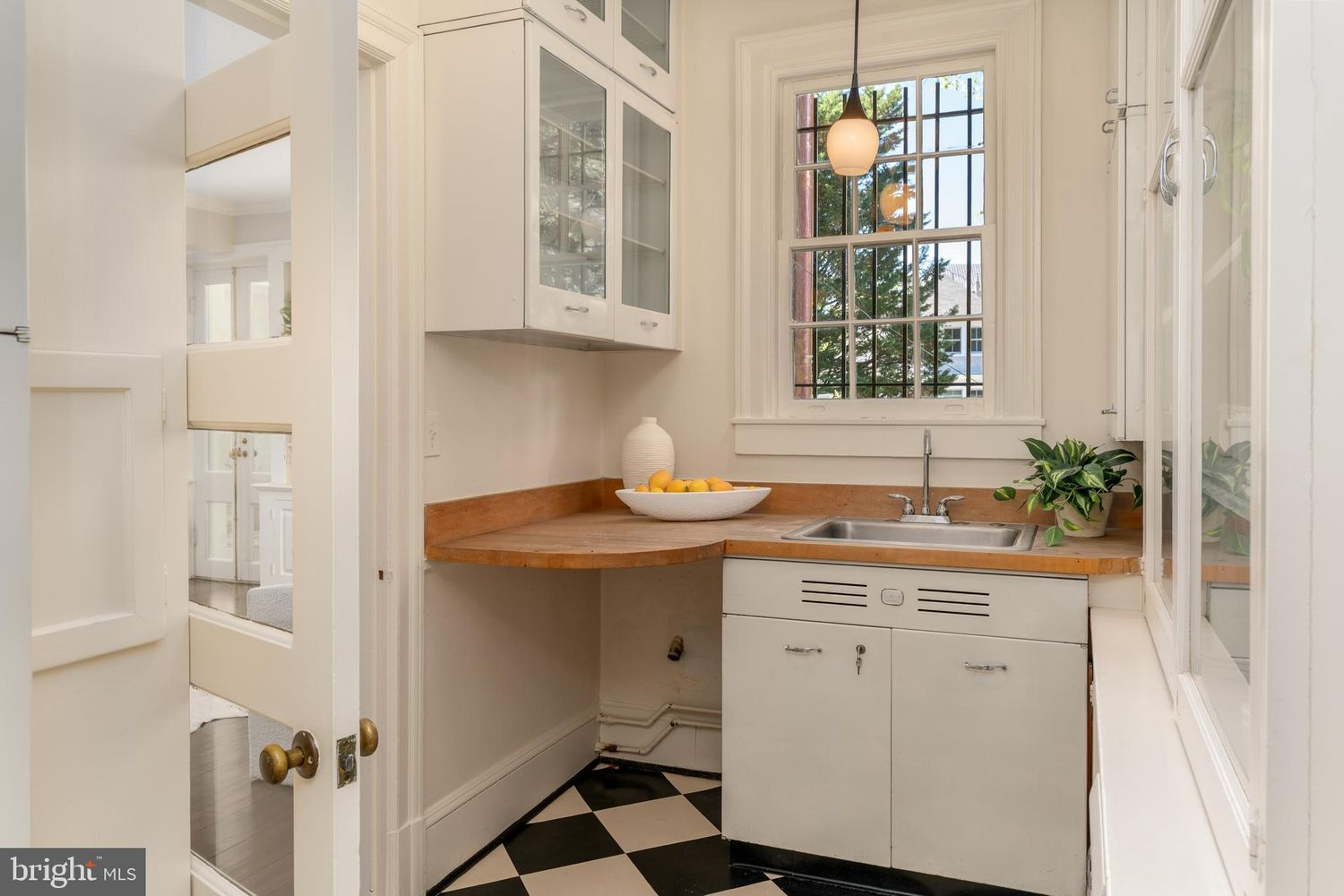 The compact room features vintage-style cabinetry with glass-front upper cabinets, warm butcher block countertops, and a small sink positioned beneath the window.