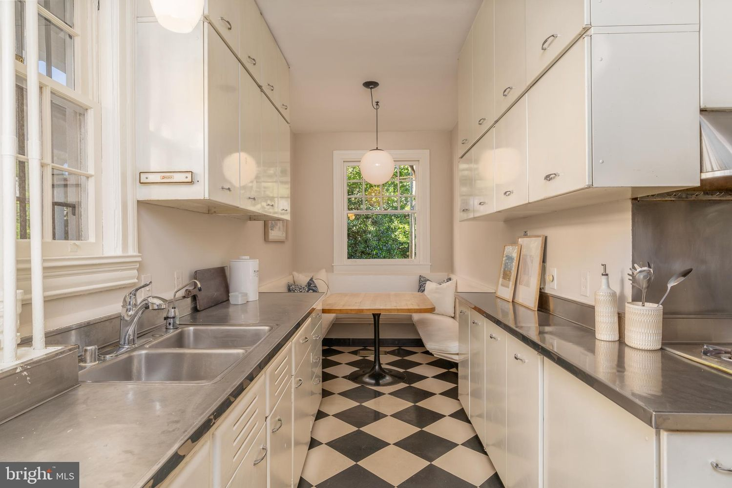 The home's kitchen lined with glossy white cabinetry stretching nearly to the ceiling on both sides, stainless steel countertops and a classic black-and-white checkered floor.