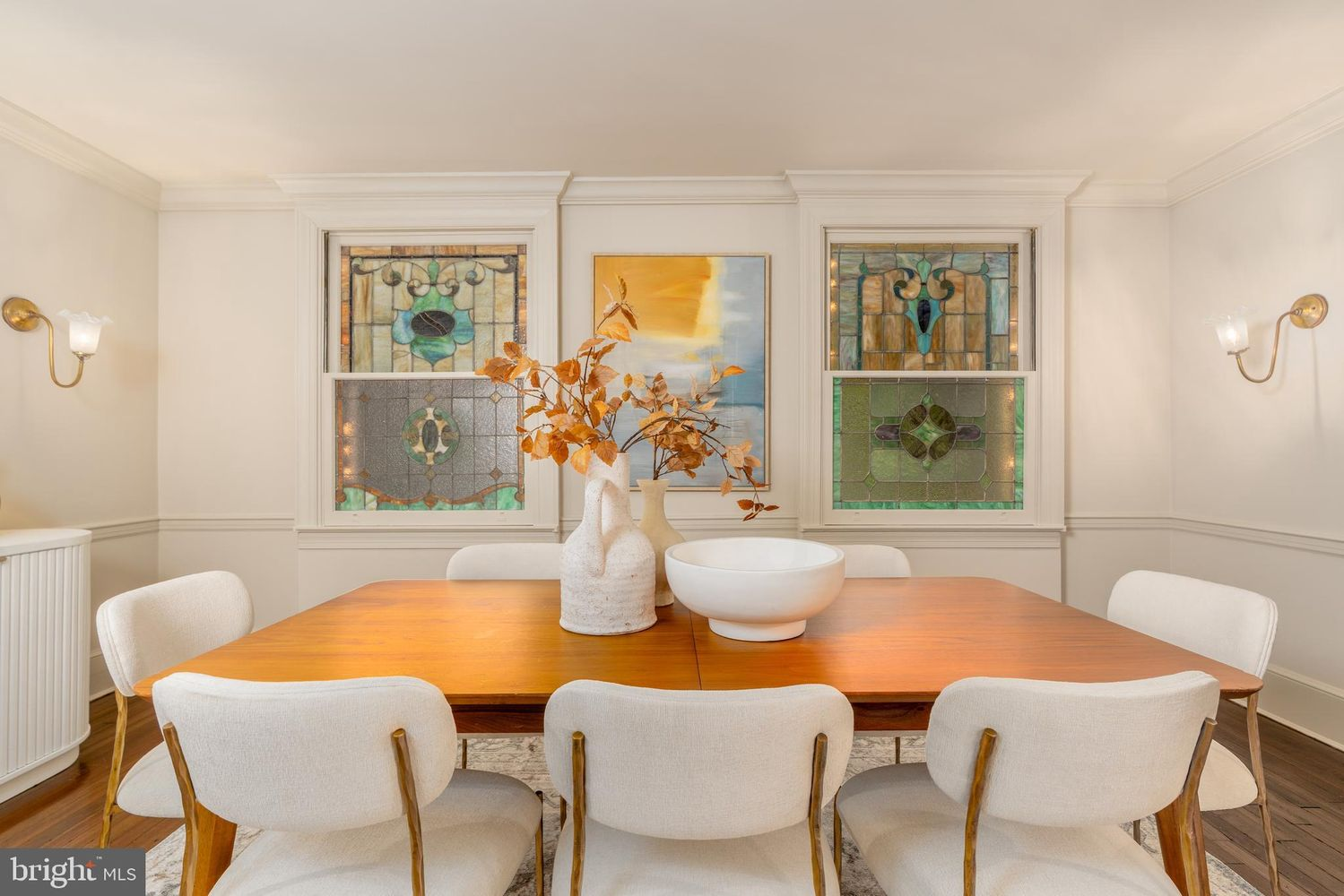 Beneath them, a large wood dining table is surrounded by white upholstered chairs that provide seating for family dinners or larger gatherings.