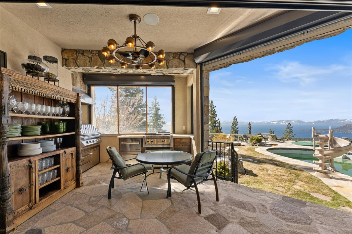 Just outside the main kitchen, retractable doors open to a covered outdoor kitchen finished in natural stone with two built-in barbecue grills and open shelving.