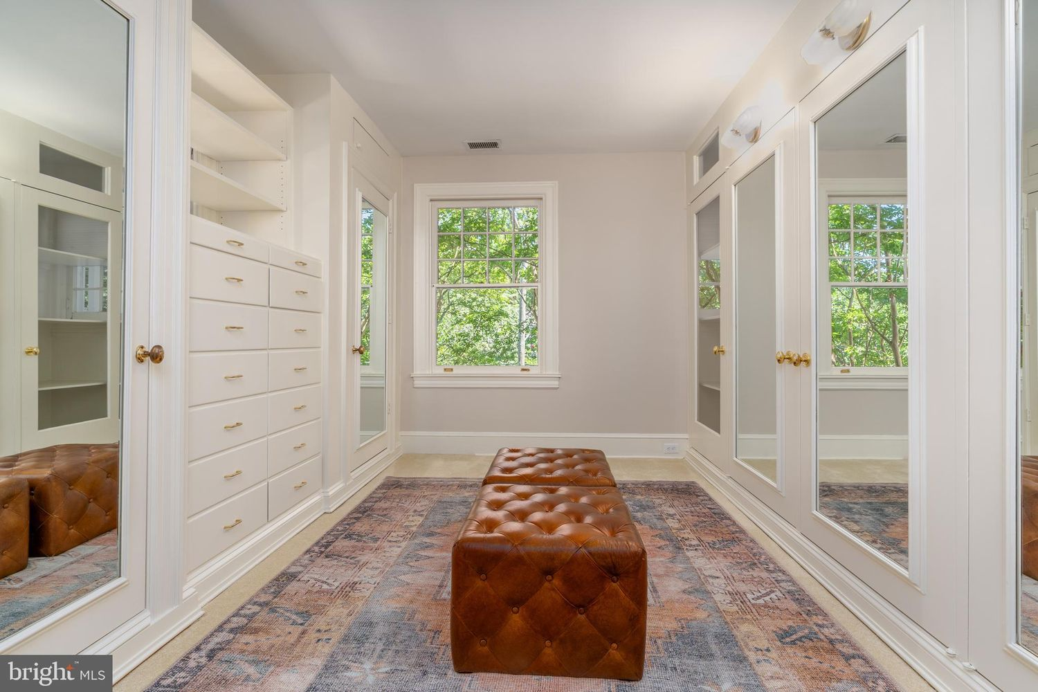 An oversized walk-in closet with custom built-in cabinetry lining both sides, combining mirrored wardrobes, banks of drawers, and open shelving.