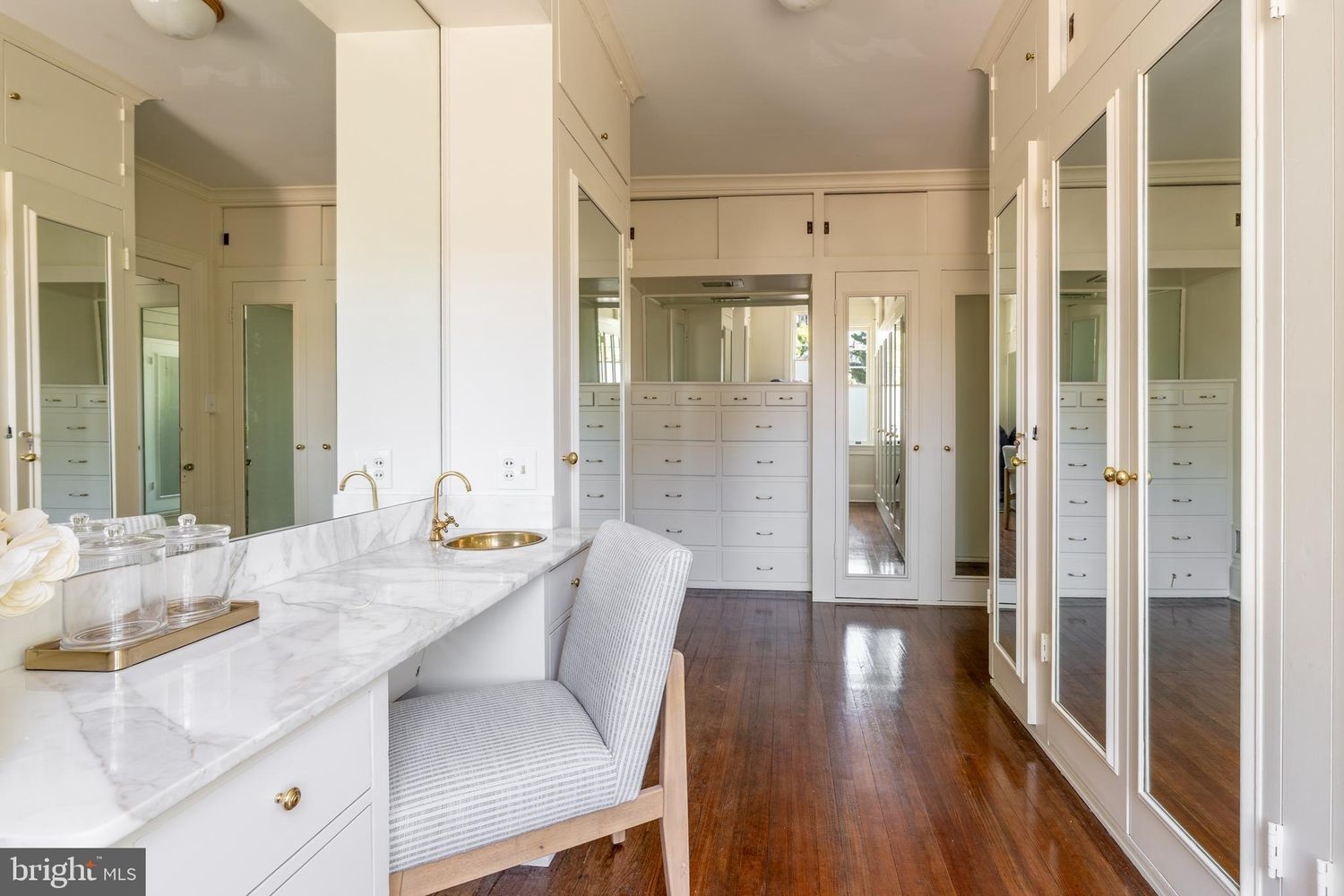 A vanity area finished with a marble countertop, integrated seating, and brass fixtures, providing a separate space for getting ready each day.