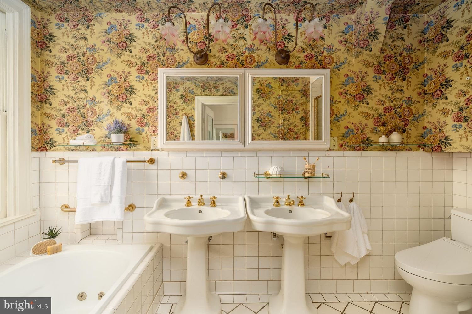 Colorful floral wallpaper wraps the upper walls, adding warmth and personality, while a soaking tub sits beside a large window.