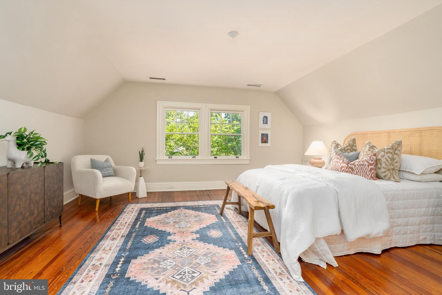 Positioned beneath the sloped roofline, this bedroom has an inviting cottage-like feel with a woven headboard, patterned area rug, and treetop views.