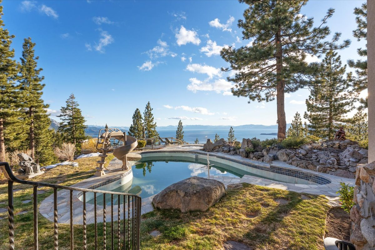 A few steps down, a freeform swimming pool is surrounded by natural boulders, mature pines, and stone patios that blend into the landscape. 