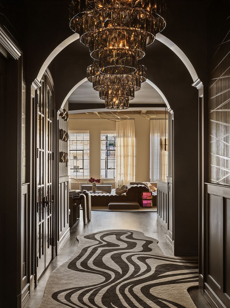 At the end of the gallery, the space opens into the main living areas, where oversized windows flood the home with natural light, creating a dramatic contrast to the moody, hotel-inspired entrance.
