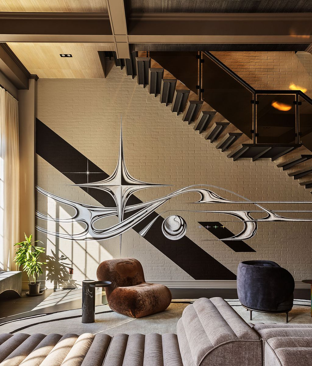 The sweeping monochromatic artwork transforms the brick wall beneath a floating staircase.