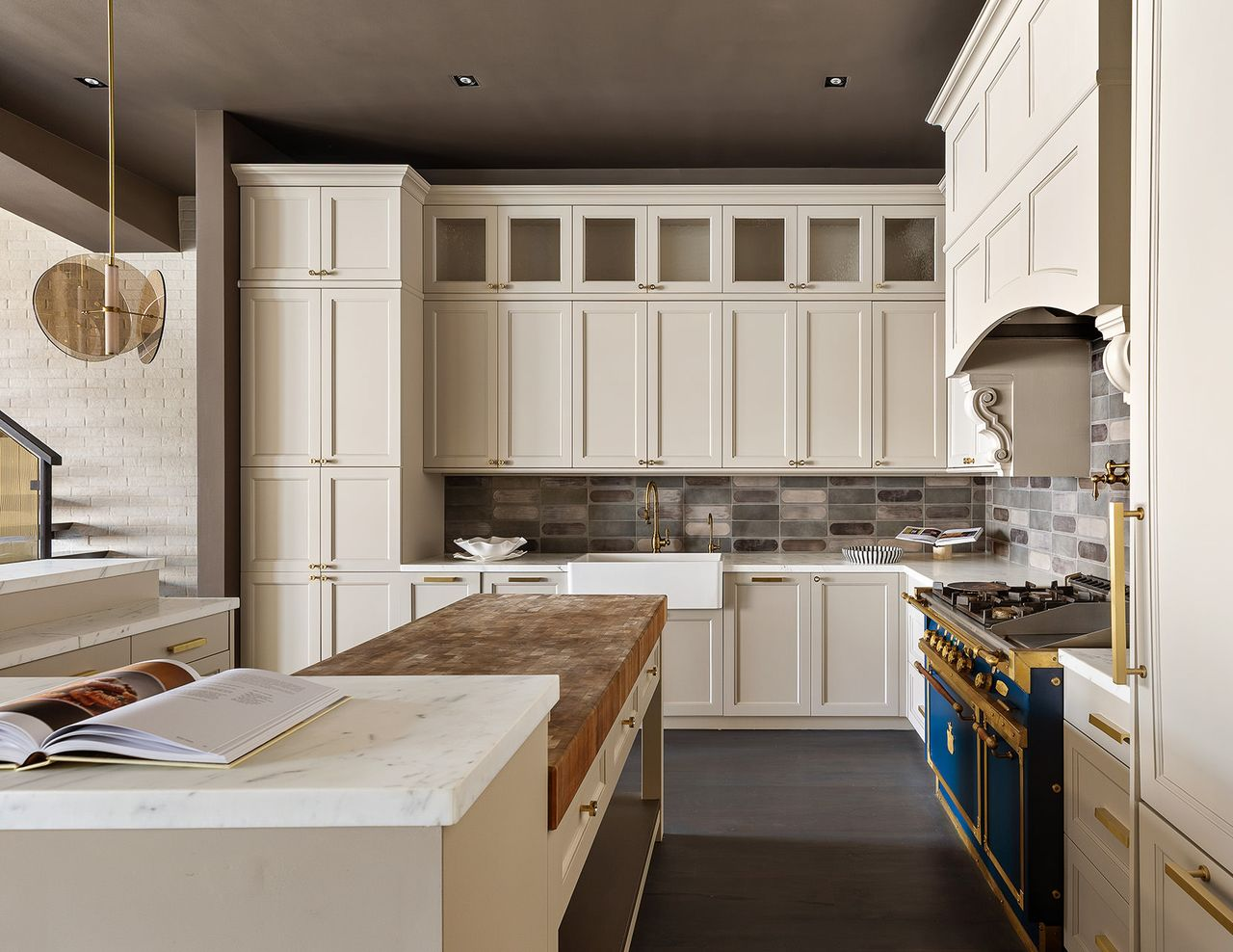 Chef's kitchen with floor-to-ceiling off-white cabinetry, marble countertops, a farmhouse sink, and a large butcher block island in the center. 