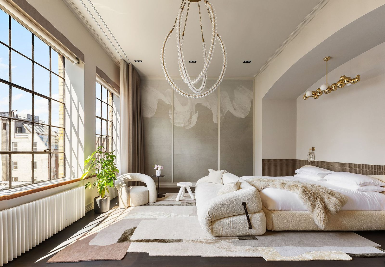 The suite's bedroom centers around a cutout wall where a custom upholstered bed sits beneath a white and gold bubble light fixture facing the windows.