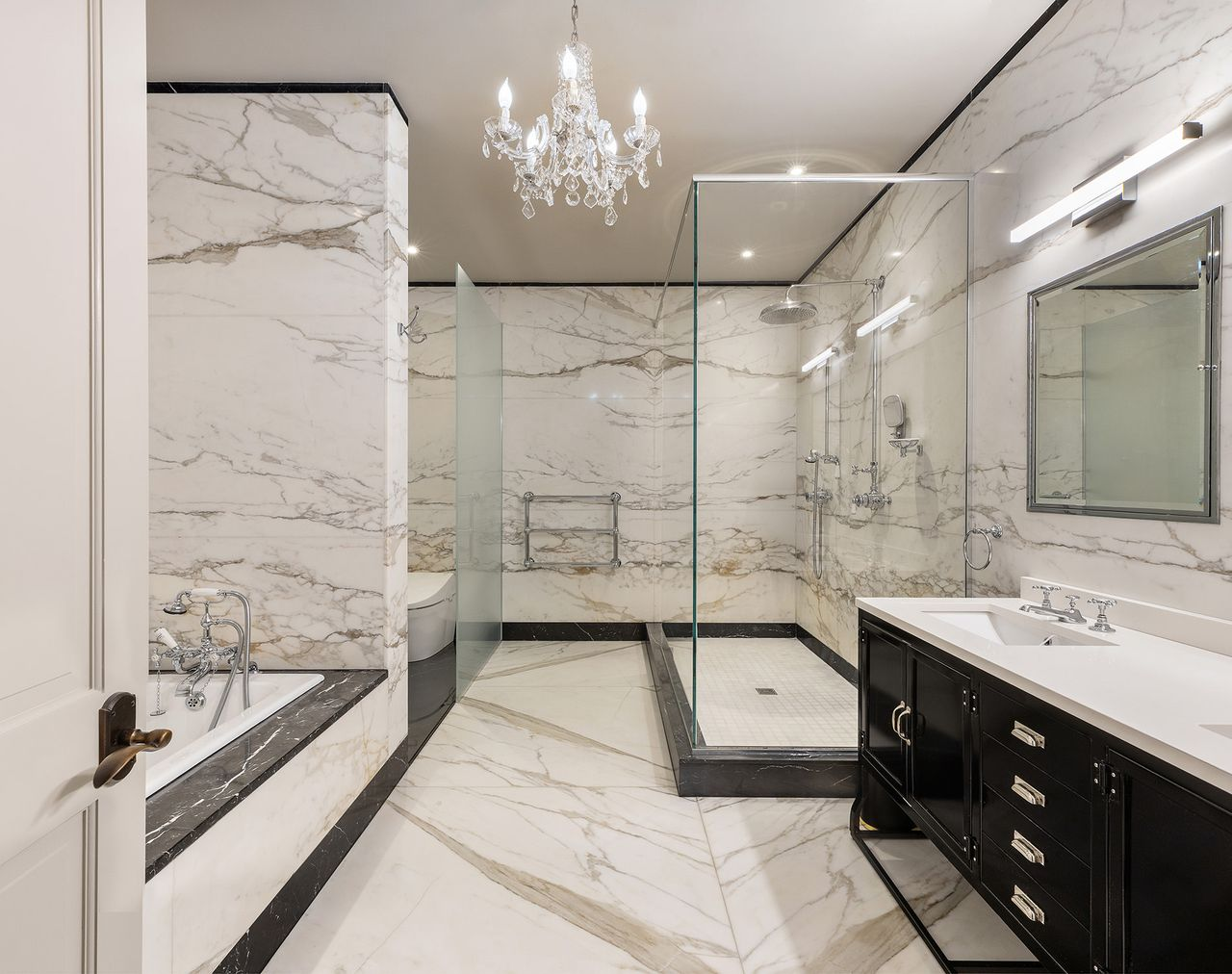 A soaking tub sits across from a walk-in glass shower equipped with multiple shower fixtures and a long double vanity. 