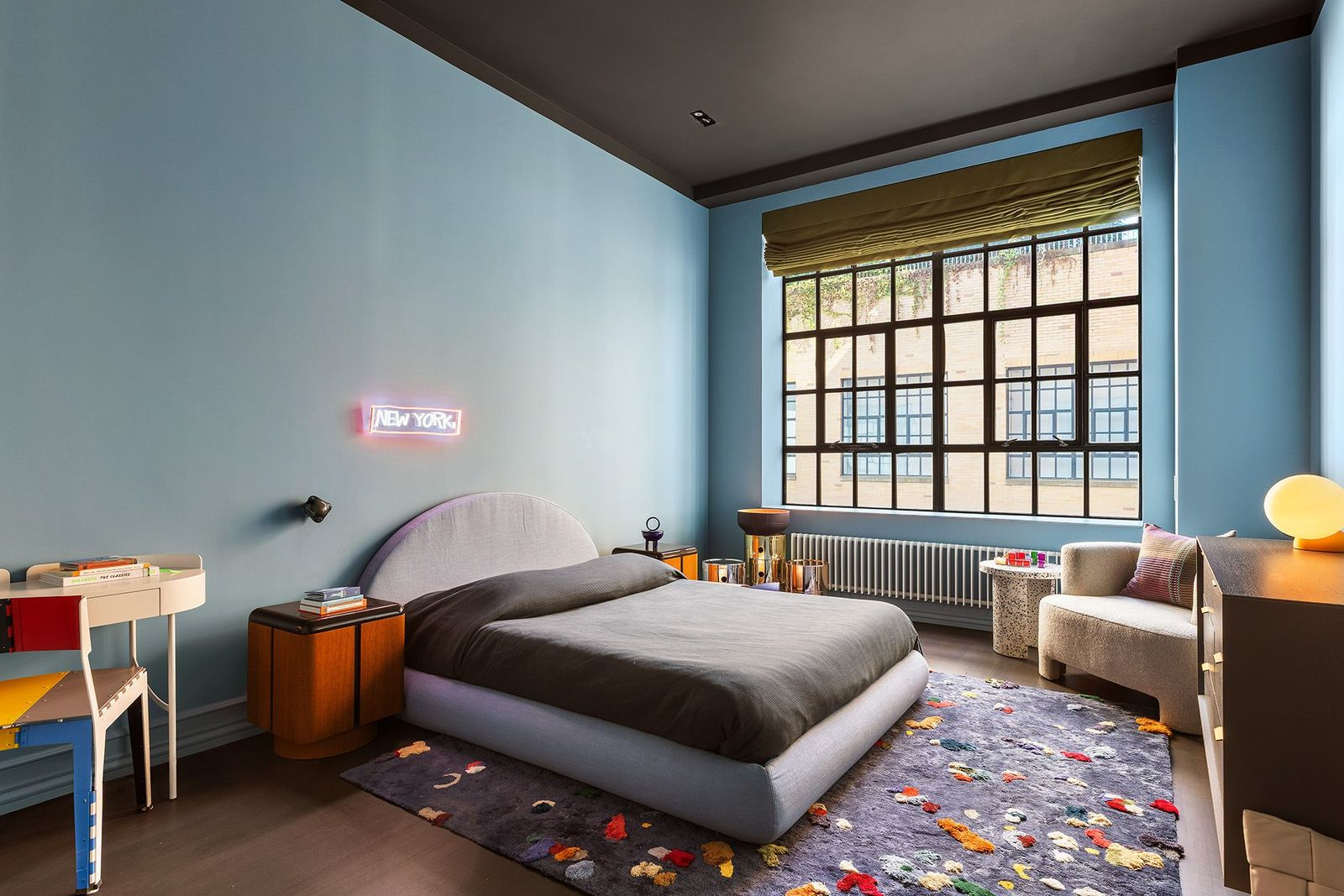 Finished in rich blue tones, the boys' bedroom balances playful details with the home's sophisticated aesthetic thanks to the rounded upholstered bed, colorful accent rug, neon "New York" sign, and reading chair tucked beside the window.