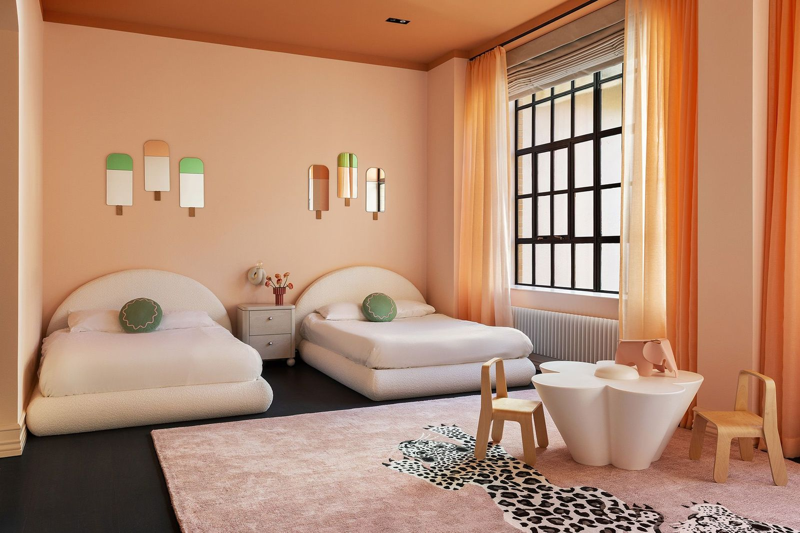 The girls' bedroom has a much softer palette with blush walls, sheer orange drapery, and oversized windows that brighten the space throughout the day. 