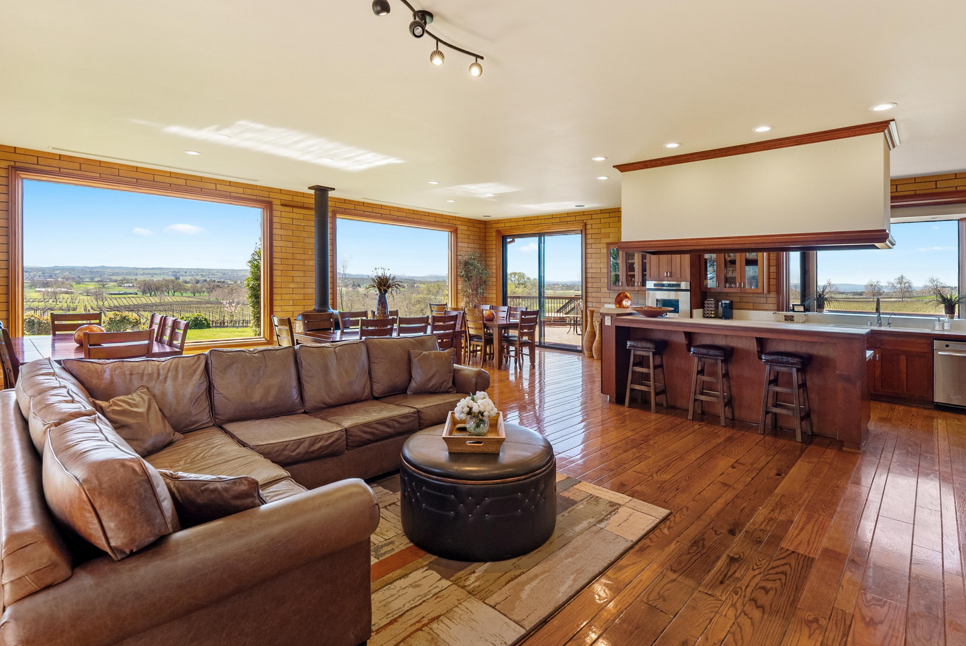 A living area centered on a large leather sectional, with hardwood floors that run continuously into the connected dining space and kitchen. 