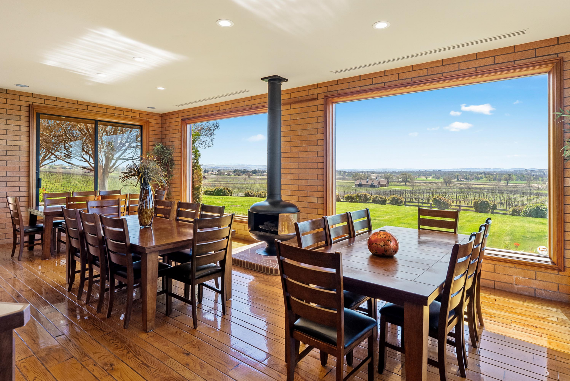 Three large dining tables sit beside a freestanding black fireplace and large picture windows.