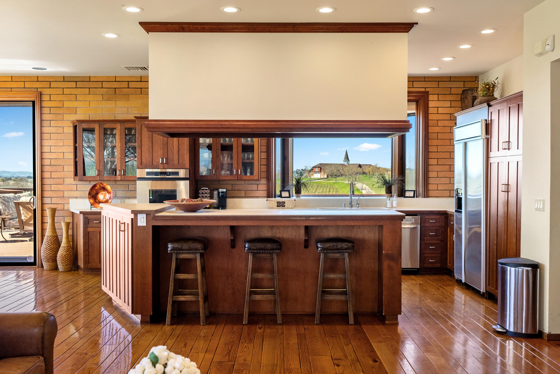 A large wood island with bartop seating for three is paired with warm wood cabinetry that stretches across the back wall around the oven.
