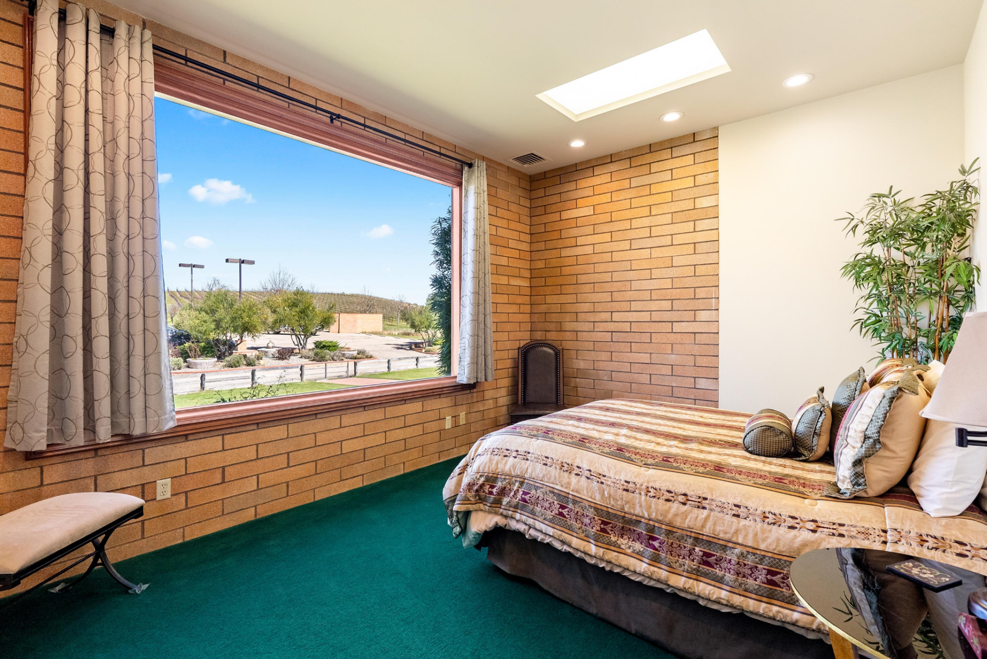 One bedroom continues the home’s brickwork across multiple walls, with a wide picture window opposite the bed and a contrasting white accent wall that breaks up the heavier masonry.
