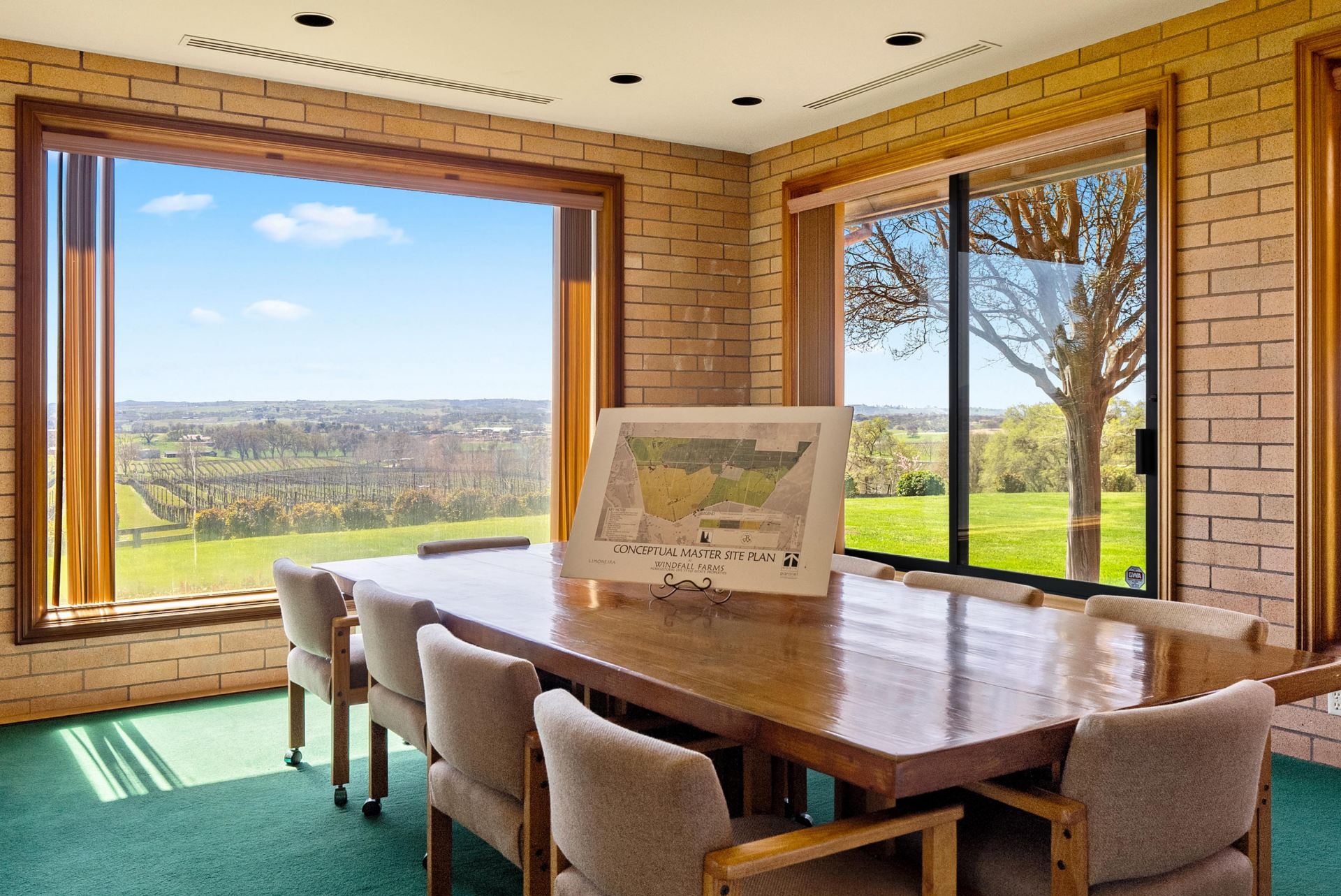 The conference room features a long wood table surrounded by cushioned rolling chairs, all set between two expansive windows.