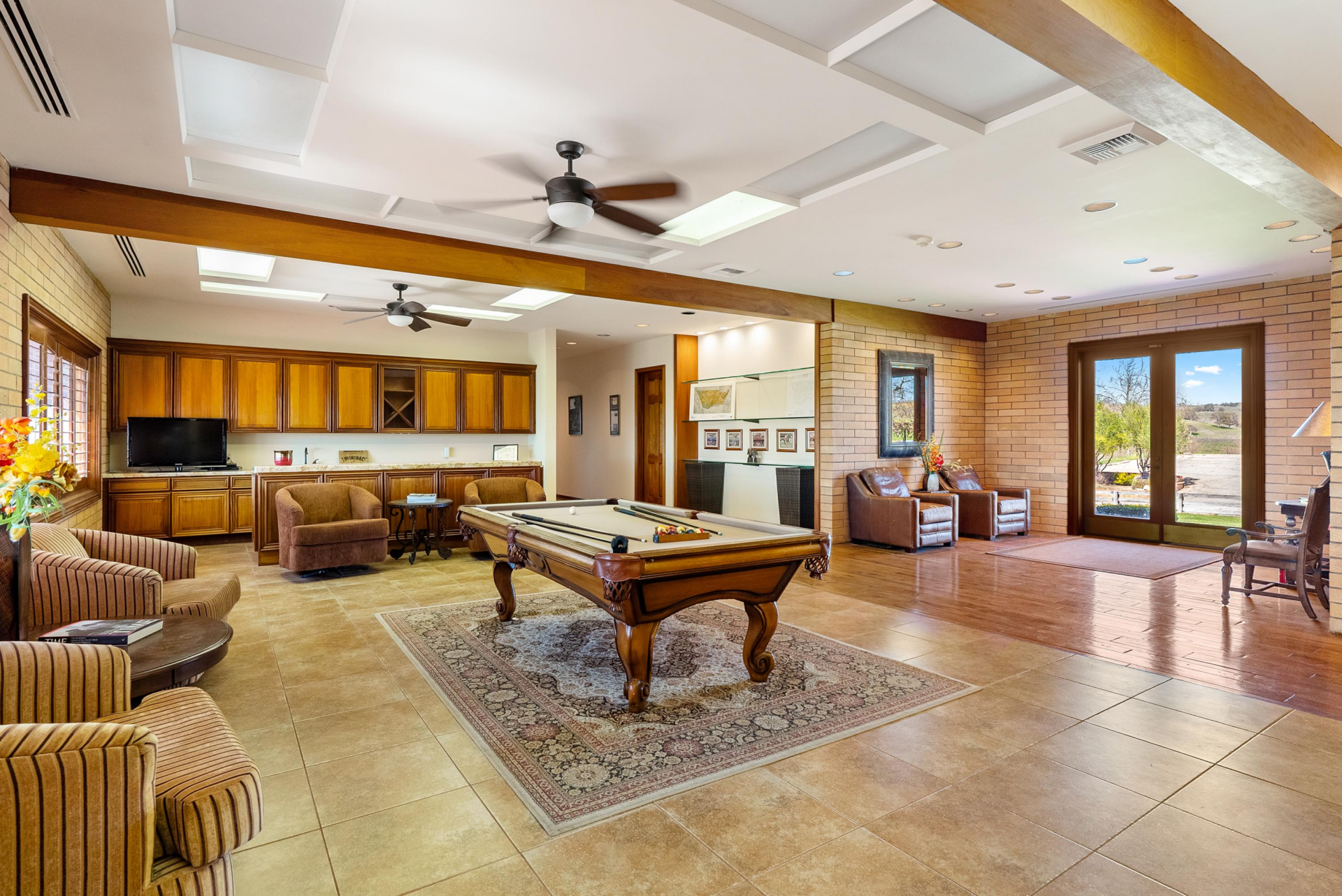 A pool table sits on one side of the room close to the wet bar lined with built-in cabinetry, and a television. 