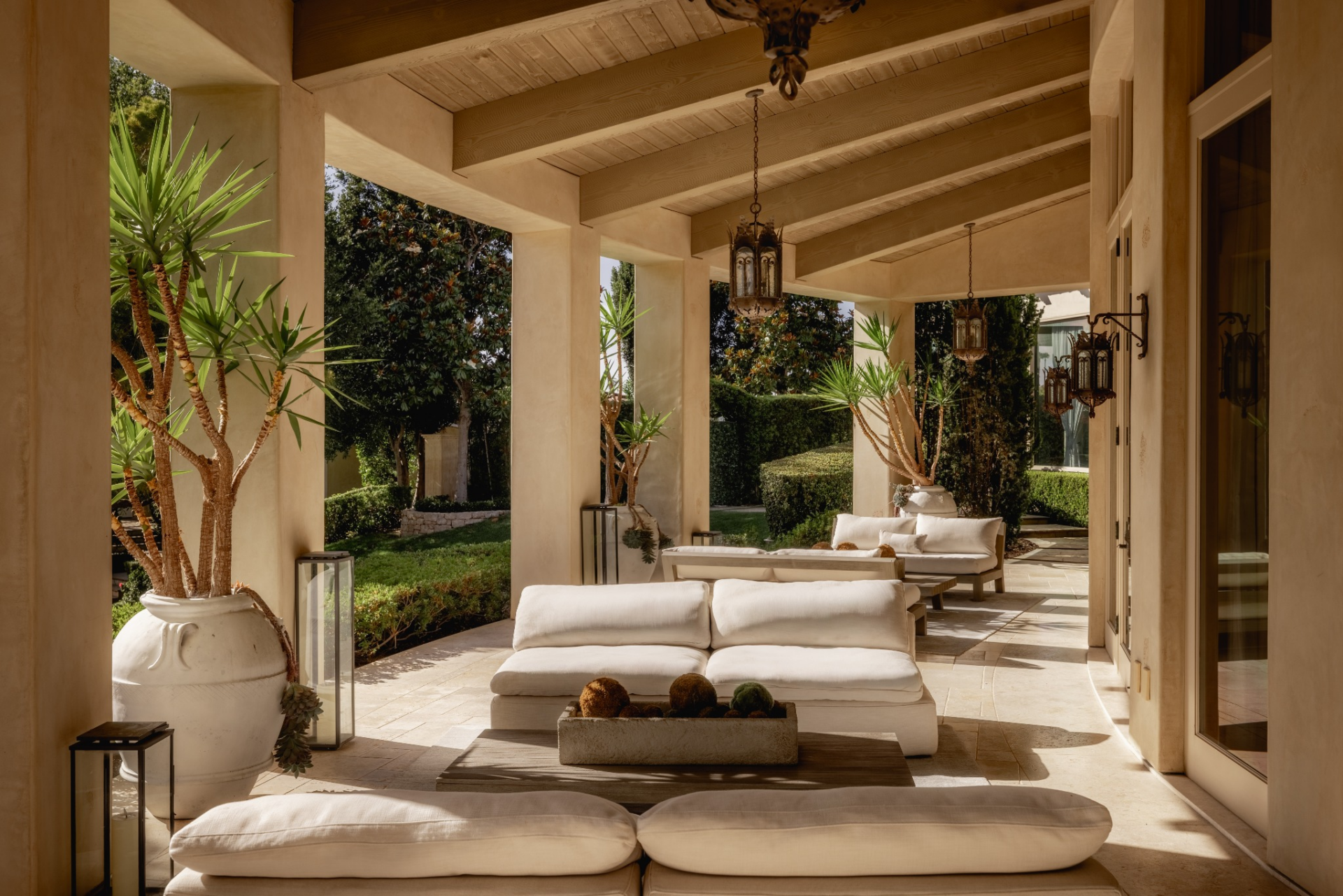 Outside the grand room, a long covered loggia runs along the residence beneath exposed wood beams and a paneled ceiling. 
