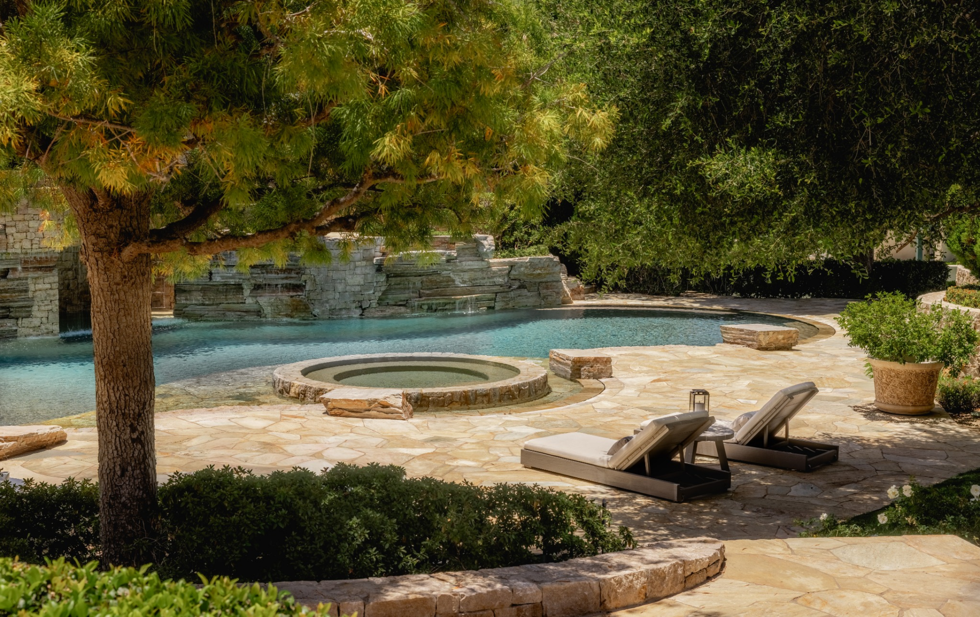 The saltwater pool is set within a broad stone terrace and shaped around a circular spa positioned near the water’s edge.
