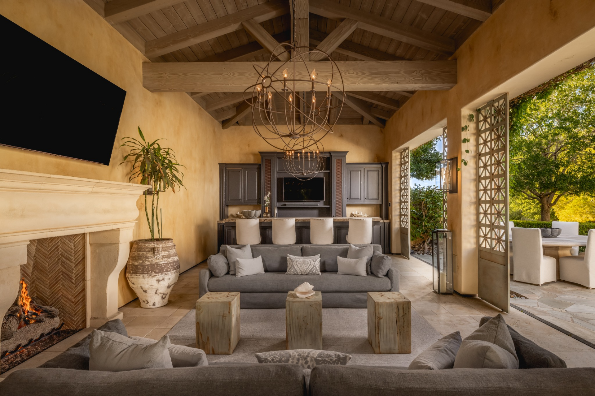 Sofas and low wood tables face a large stone fireplace and wall-mounted television, while a full bar stretches across the back of the room.