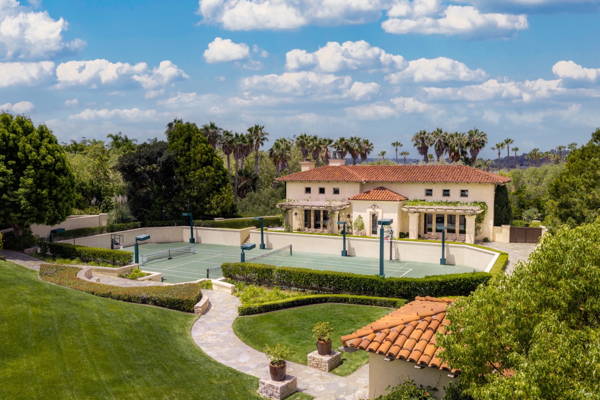 A separate multi-sport complex combines tennis, basketball, and pickleball within a sunken court bordered by trimmed hedges and stone pathways.